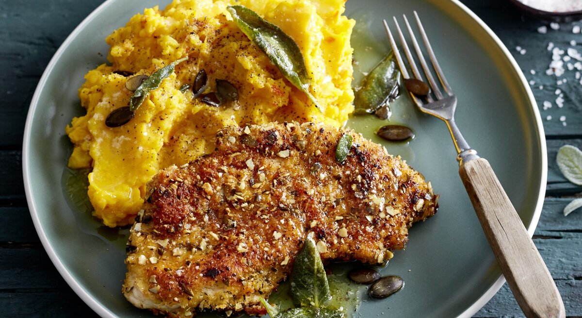 Knusper-Schnitzel mit Kürbisstampf auf Teller, belegt mit Salbei und Kürbiskernen. 