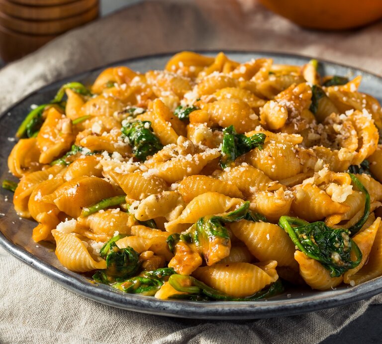 Ein grauer Teller mit der Pasta auf einem hellgrauen Tuch. Dahinter frischer Kürbis und Gewürzstreuer. Alles von der Seite fotografiert. | © Shutterstock/ Brent Hofacker 