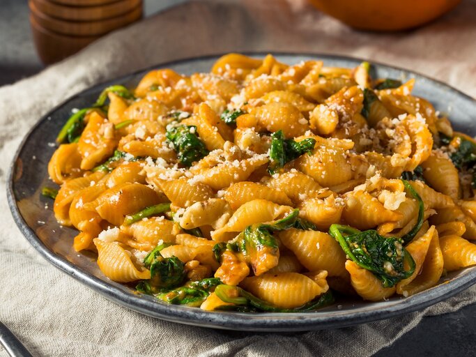 Ein grauer Teller mit der Pasta auf einem hellgrauen Tuch. Dahinter frischer Kürbis und Gewürzstreuer. Alles von der Seite fotografiert. | © Shutterstock/ Brent Hofacker 