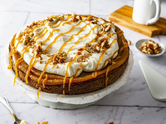 Kürbiskuchen mit Frischkäsecreme und gebrannten Walnüssen, garniert mit Karamell und serviert auf einer großen Kuchenplatte auf einem weißen Fliesentisch.  | © StockFood / Krimshandl-Tauscher, Sandra