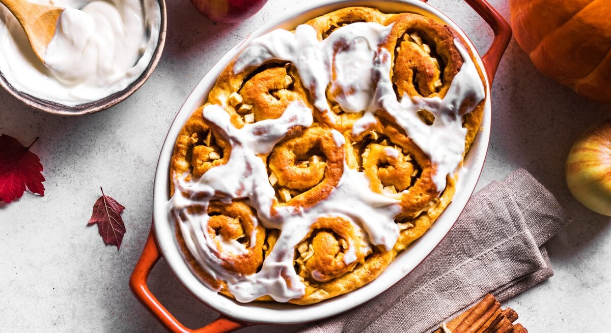 Kürbis-Zimtschnecken mit Guss in roter Auflaufform auf hellem Untergrund. 