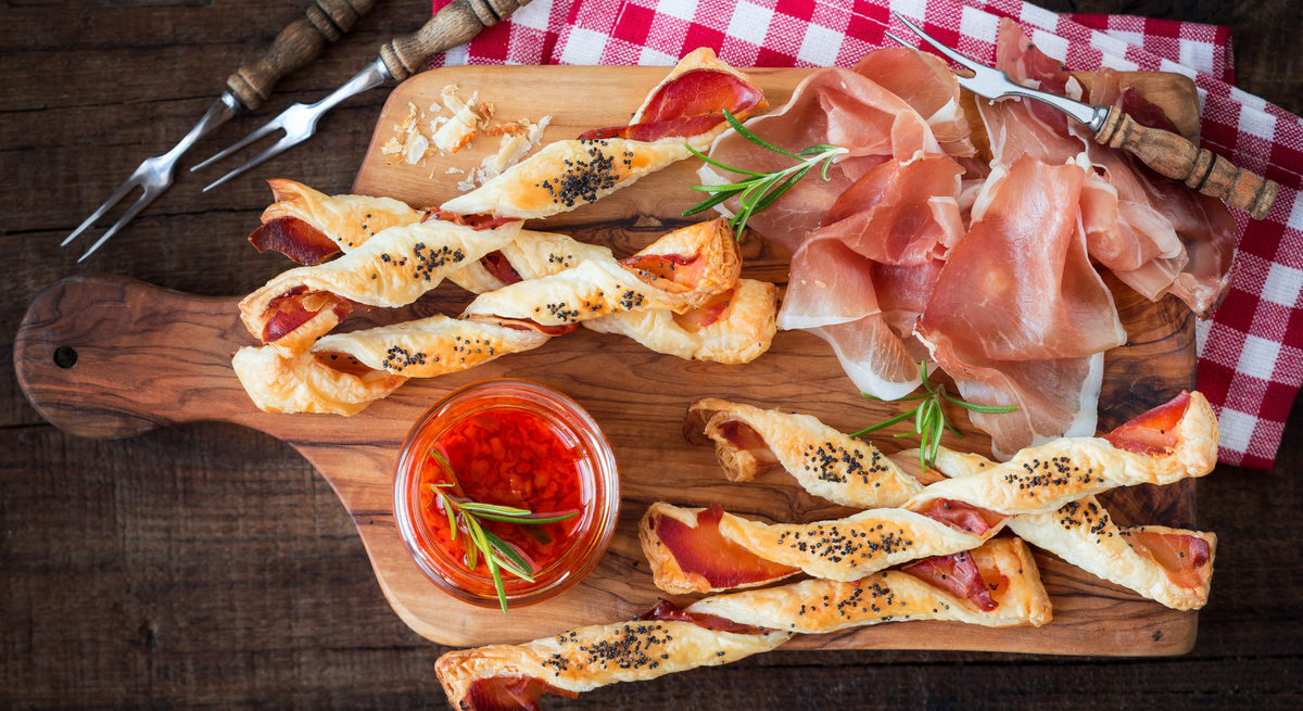 Kalorienarme Pizzastangen aus Skyr auf Holzbrett, daneben Parmaschinken und Gabeln