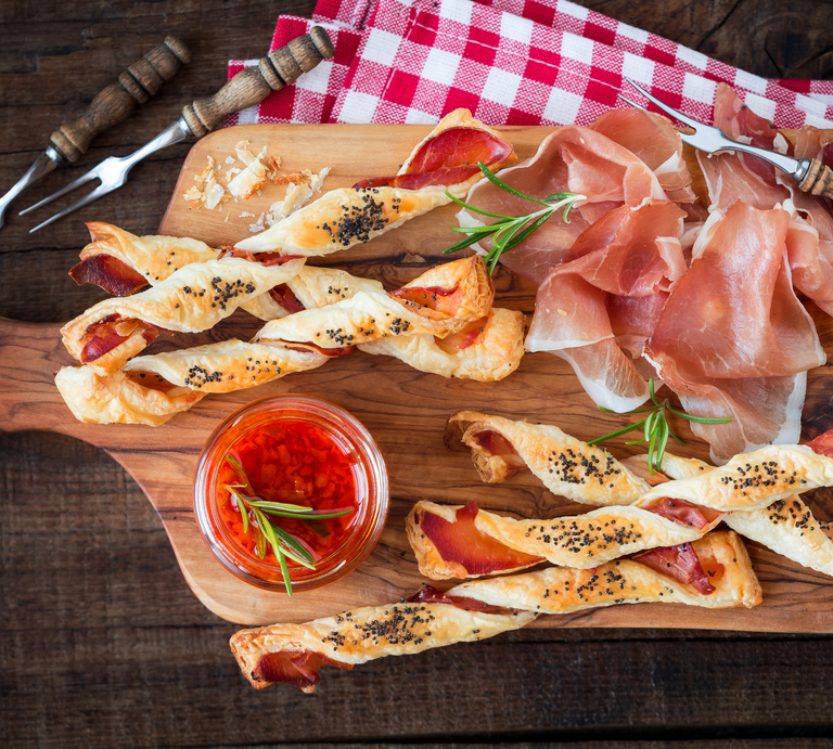Kalorienarme Pizzastangen aus Skyr auf Holzbrett, daneben Parmaschinken und Gabeln | © Getty Images/ Kuvona
