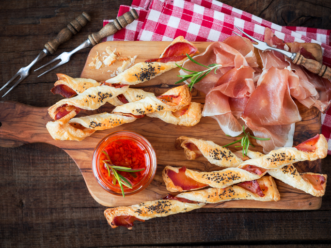 Kalorienarme Pizzastangen aus Skyr auf Holzbrett, daneben Parmaschinken und Gabeln | © Getty Images/ Kuvona