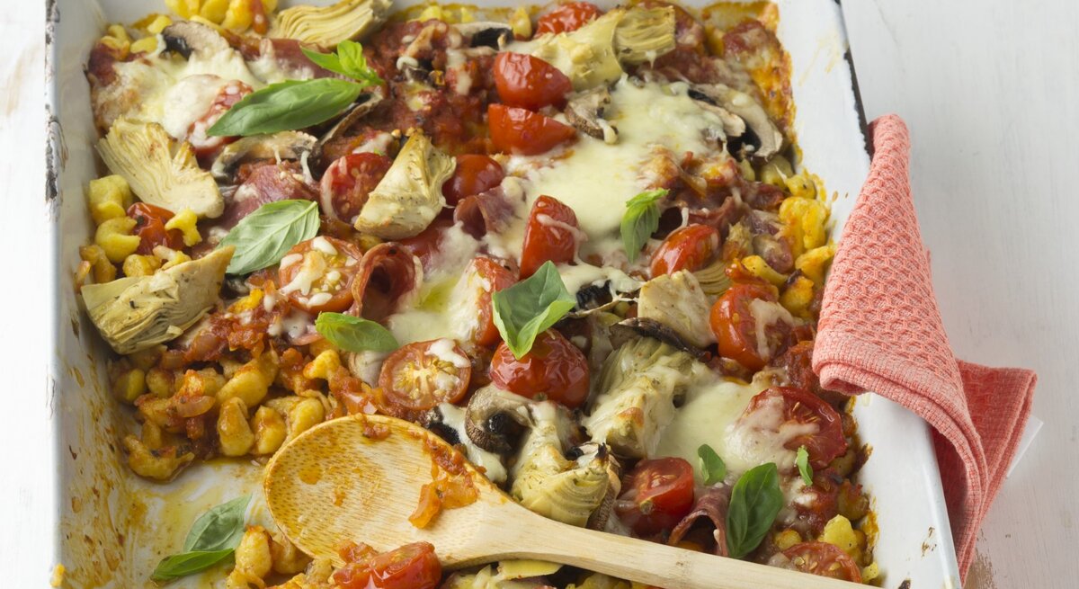 Überbackene Pizza-Spätzle mit Pilzen, Salami und Tomatensoße in einer quadratischen weißen Auflaufform. 