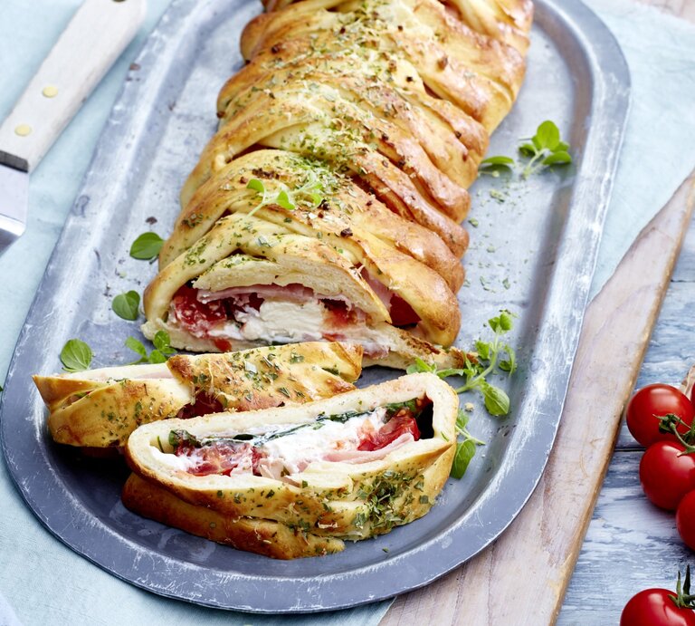Auf einem Teller ist eine Pizzarolle „Stromboli“ angerichtet. Sie ist mit Aufschnitt gefüllt und mit Kräutern verfeinert. | © EAT CLUB / Isabell Triemer