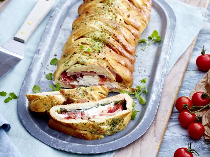 Auf einem Teller ist eine Pizzarolle „Stromboli“ angerichtet. Sie ist mit Aufschnitt gefüllt und mit Kräutern verfeinert. | © EAT CLUB / Isabell Triemer