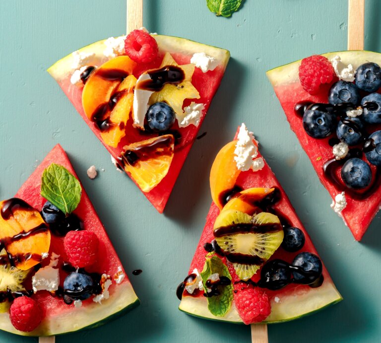 Vier Stücken Wassermelone, belegt mit Obst auf einem grünem Tisch. Alles direkt von oben fotografiert. | © Shutterstock/ Tanya Sid
