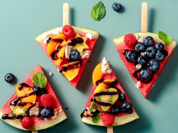 Vier Stücken Wassermelone, belegt mit Obst auf einem grünem Tisch. Alles direkt von oben fotografiert. | © Shutterstock/ Tanya Sid
