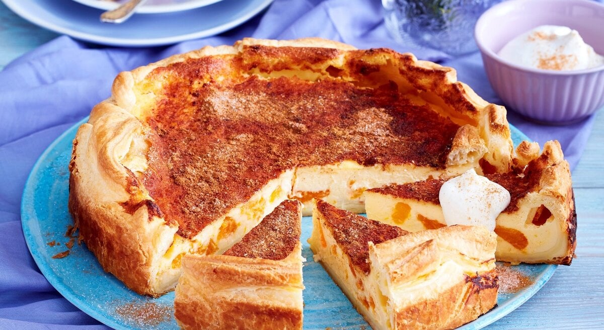 Auf einem blauen Teller liegt ein Blätterteig-Schmand-Kuchen. Er ist mit einem Klecks Sahne bedeckt.