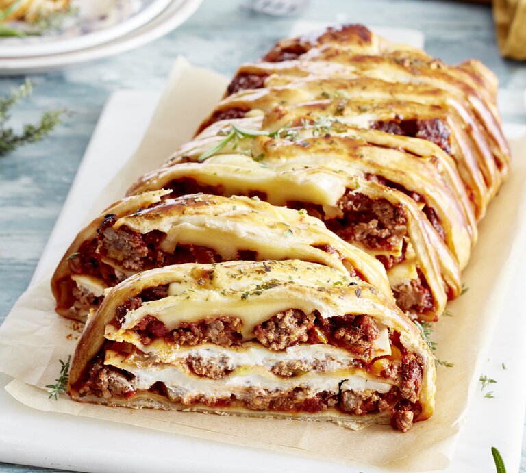 Ein Lasagne-Blätterzopf auf einem weißen Teller auf hellblauem Tisch. | © EAT CLUB/Isabell Triemer