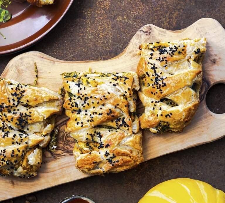 Auf einem Schneidebrett liegt Blätterteiggebäck gefüllt mit Kürbis, Spinat und Feta. Es ist mit Sesam bestreut. | © StockFood / Thorpe, Lara Jane