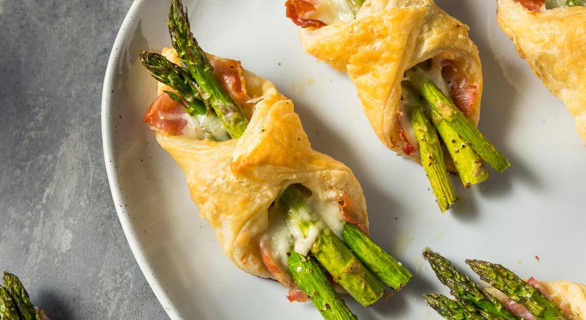 Spargel-Päckchen mit Schinken und Käse auf weißem Teller. 