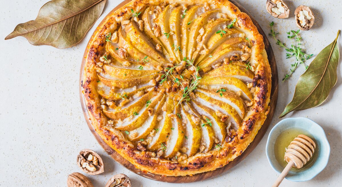 Walnuss-Birnentarte mit Blätterteig mit herbstlicher Dekoration auf weißem Untergrund. 