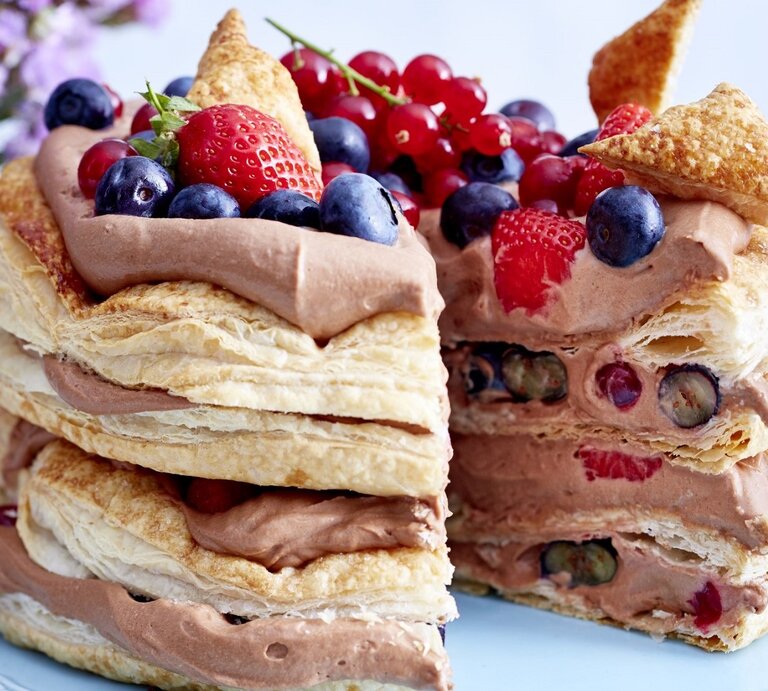 Auf einem Teller steht eine Schoko-Beeren-Torte. Sie hat mehrere Schichten Creme und ist mit verschiedenen Beeren dekoriert. | © EAT CLUB / Isabell Triemer