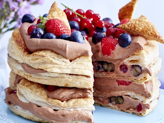 Auf einem Teller steht eine Schoko-Beeren-Torte. Sie hat mehrere Schichten Creme und ist mit verschiedenen Beeren dekoriert. | © EAT CLUB / Isabell Triemer