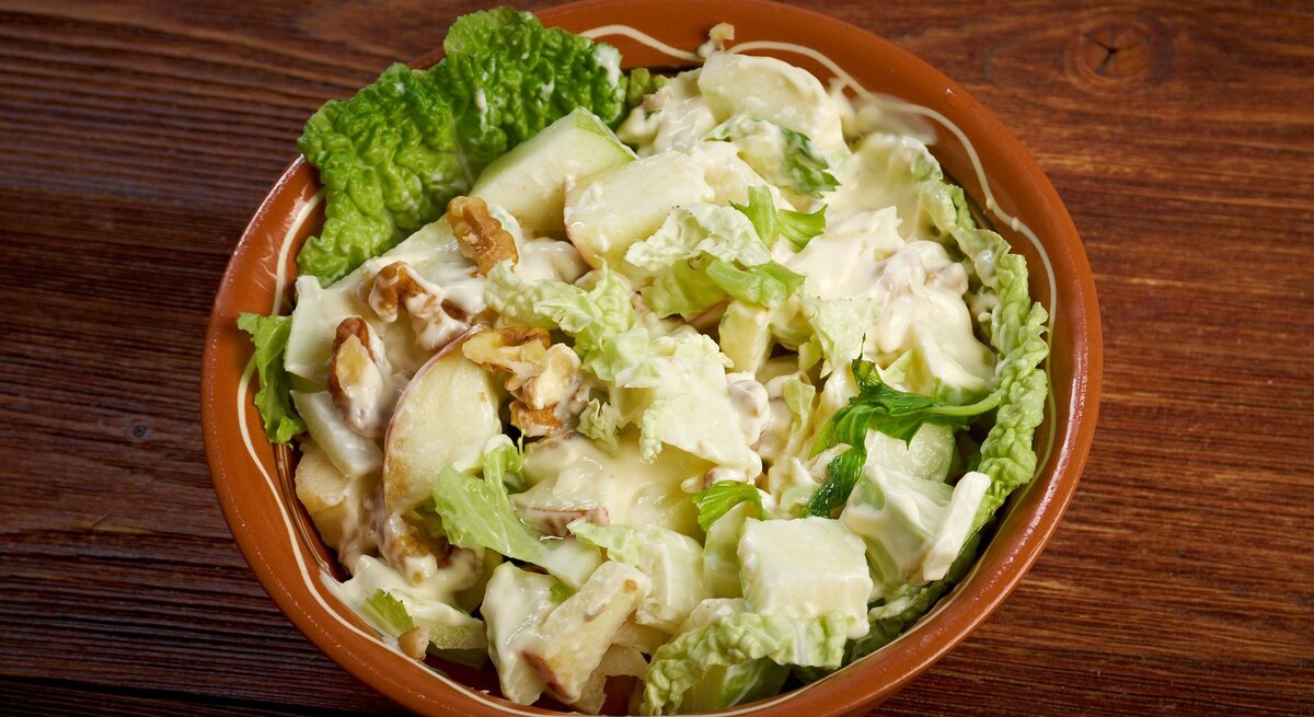 Eine braune Schale mit dem Salat auf einem dunklen Holztisch von oben fotografiert.