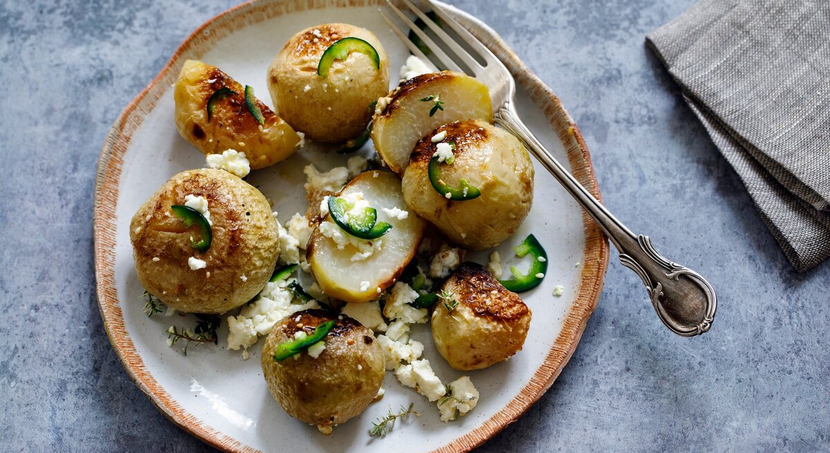 Teller auf hellblauem Untergrund belegt mit gebackenem Kohlrabi mit Feta. Daneben liegen eine Gabel und eine Serviette. 