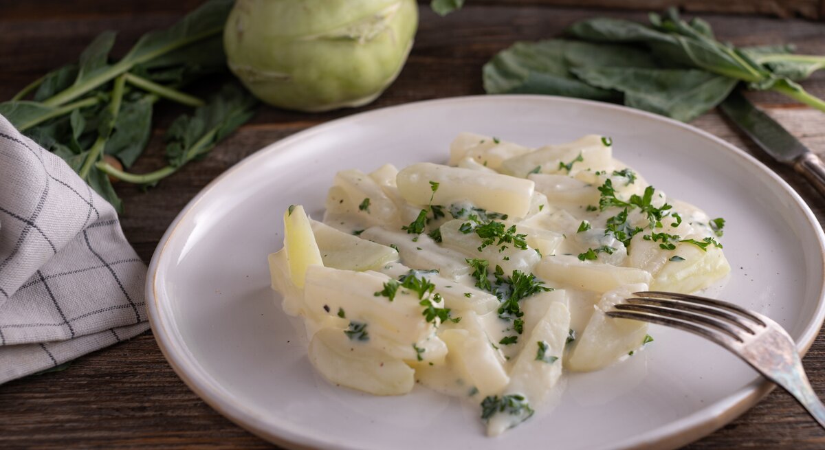 Weißer Teller belegt mit Rahmkohlrabi auf hölzernem Untergrund. 