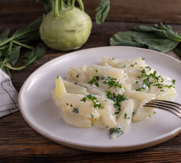 Weißer Teller belegt mit Rahmkohlrabi auf hölzernem Untergrund.  | © Getty Images/Angelika  Heine