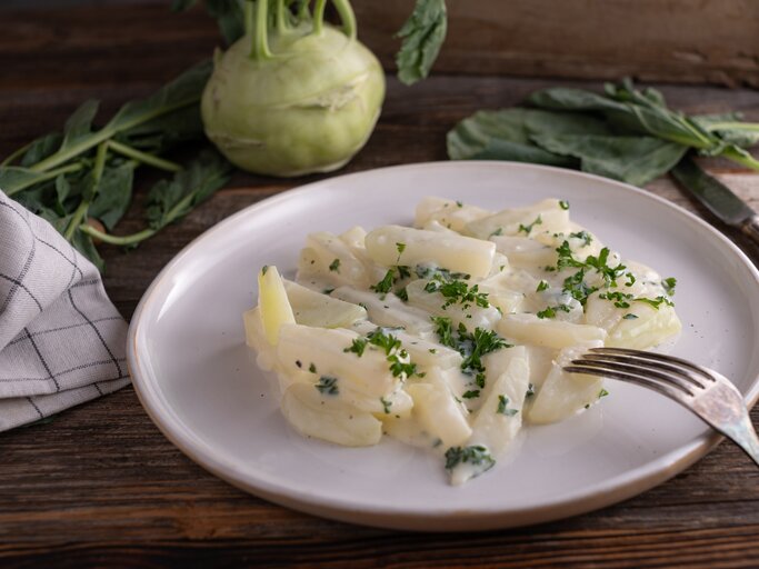 Weißer Teller belegt mit Rahmkohlrabi auf hölzernem Untergrund.  | © Getty Images/Angelika  Heine