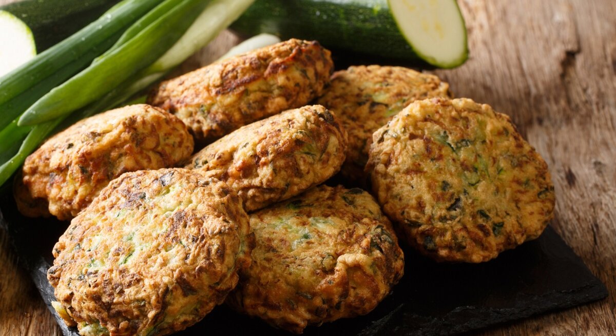 Eine schwarze Schieferplatte mit Zucchini-Feta-Kugeln oben drauf.