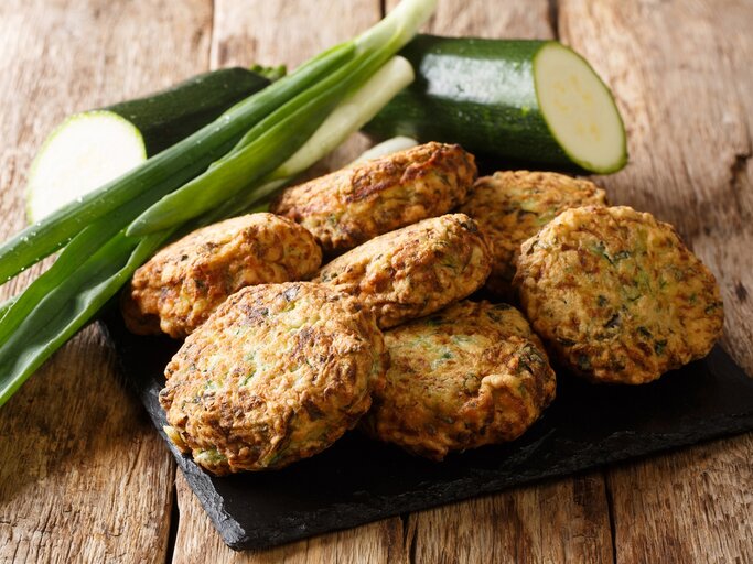 Eine schwarze Schieferplatte mit Zucchini-Feta-Kugeln oben drauf. | © GettyImages/ALLEKO