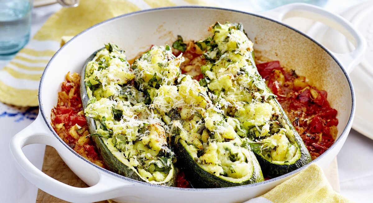 gefüllte Zucchini-Boote mit Kartoffelfüllung auf Tomatengemüse in einer runden Auflaufform.