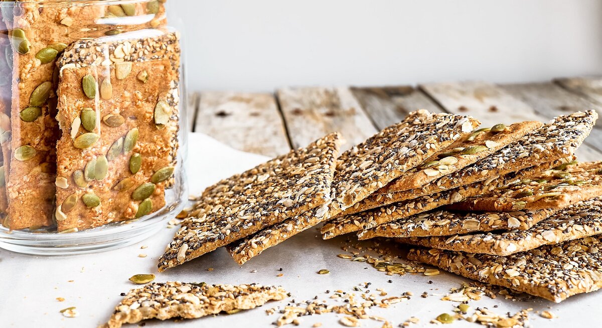 Mehrere Knäckebrote auf einem Holztisch mit Backpapier und einem Glas mit dem Knäckebrot.