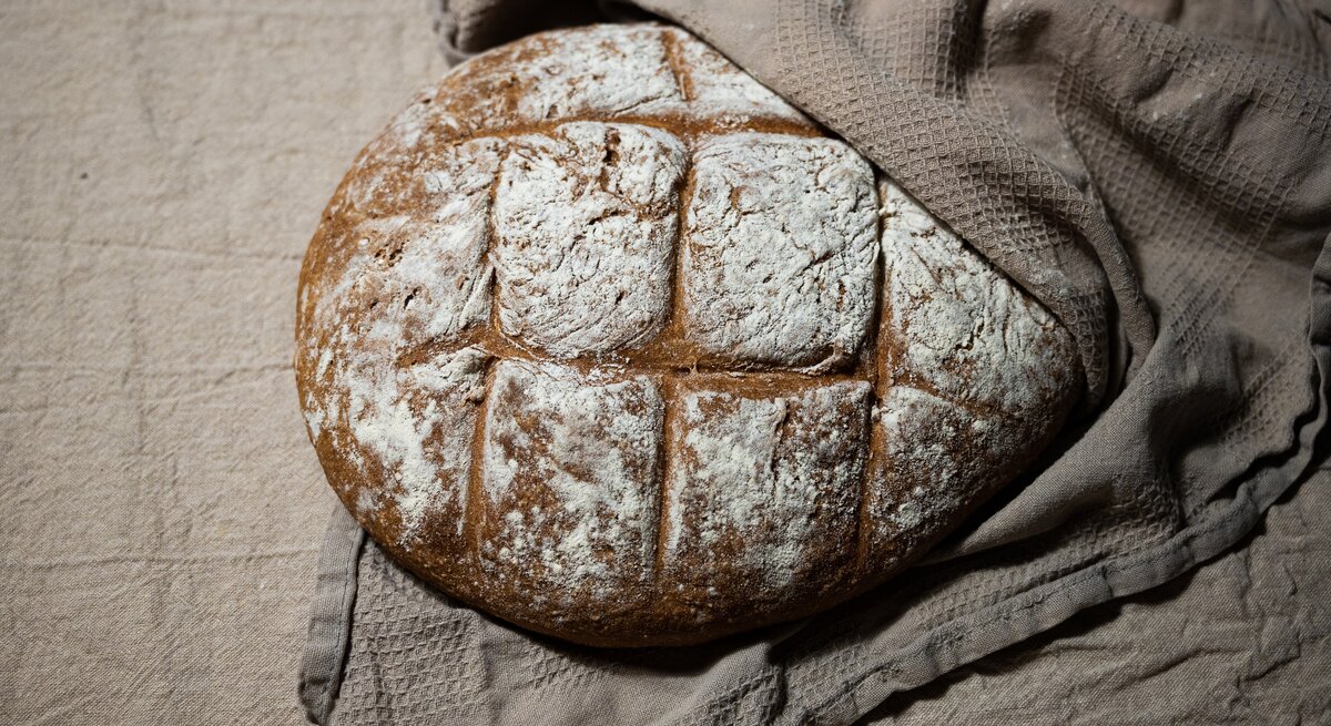 Draufsicht, schräg: Ein Hopfenbrot, das zu Hälfte in einem brauen Leinentuch eingeschlagen ist.