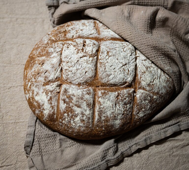 Draufsicht, schräg: Ein Hopfenbrot, das zu Hälfte in einem brauen Leinentuch eingeschlagen ist. | © Shutterstock / Marvin Glodek
