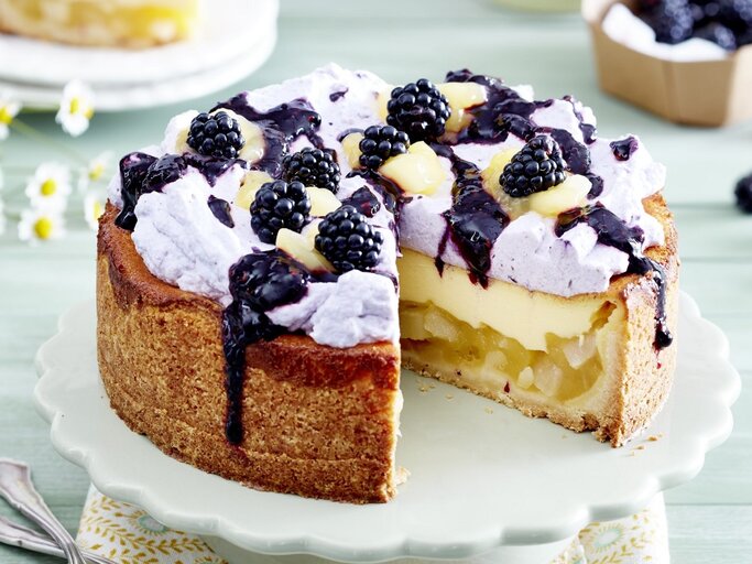 Auf einem Teller steht eine Birnen-Brombeer-Schmandtorte. Sie ist mit einer lila Creme verziert und mit Früchten bedeckt. Darüber wurde eine Brombeersoße gegeben.  | © EAT CLUB / Isabell Triemer