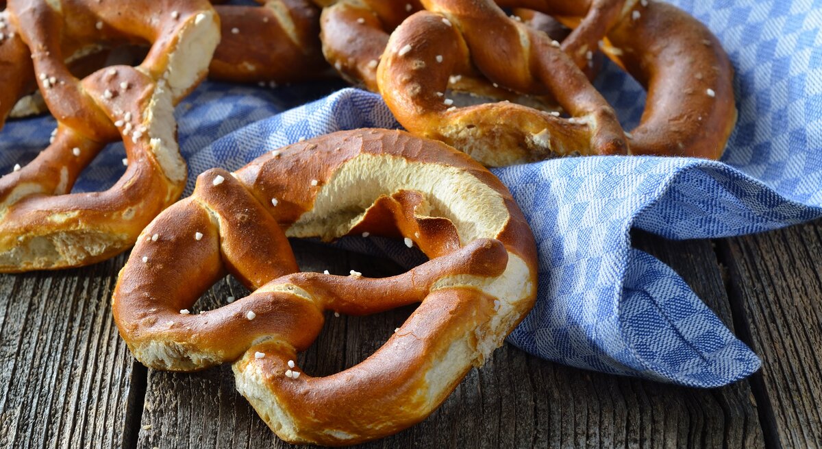 Draufsicht: Auf einem Holutisch liegen frische bayerische Brezen azf einem groben weiß-blau kariertem Tuch.