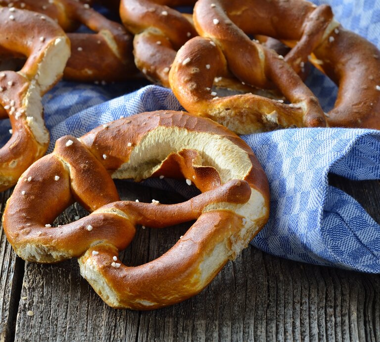 Draufsicht: Auf einem Holutisch liegen frische bayerische Brezen azf einem groben weiß-blau kariertem Tuch. | © Shutterstock / Karl Allgaeuer