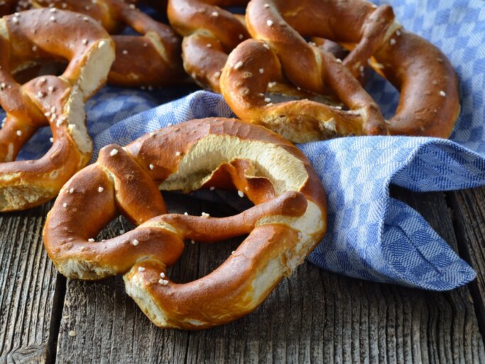 Draufsicht: Auf einem Holutisch liegen frische bayerische Brezen azf einem groben weiß-blau kariertem Tuch. | © Shutterstock / Karl Allgaeuer