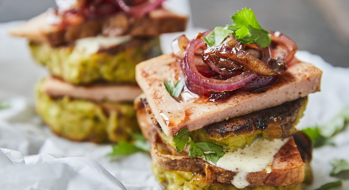 Knödelburger mit Leberkäse und roten Zwiebeln stehen auf Backpapier. 