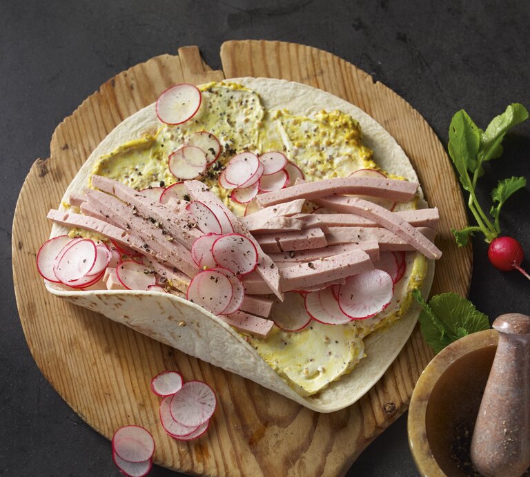 Bayern-Wraps mit Leberkäse, Senfcreme und Radieschen, garniert mit frischem Pfeffer und serviert auf einem runden Holzbrett.  | © StockFood / für ZS Verlag / Westermann, Jan-Peter