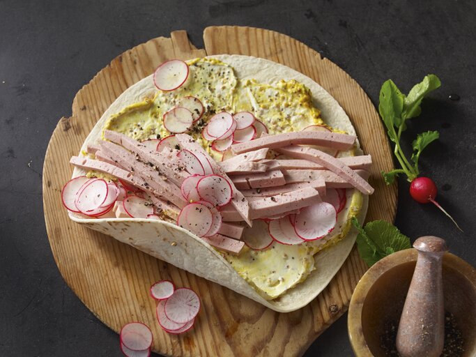 Bayern-Wraps mit Leberkäse, Senfcreme und Radieschen, garniert mit frischem Pfeffer und serviert auf einem runden Holzbrett.  | © StockFood / für ZS Verlag / Westermann, Jan-Peter