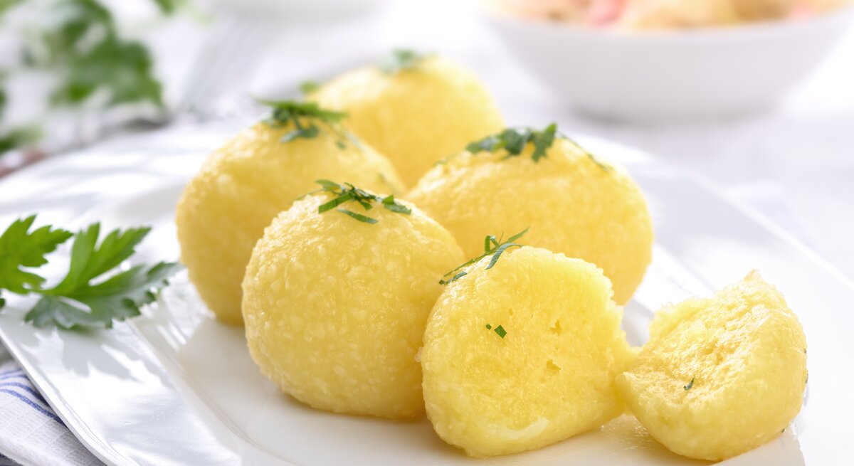 Auf einem weißen Teller liegen mehrere hausgemachte Kartoffelknödel, die mit Petersilie bestreut sind.