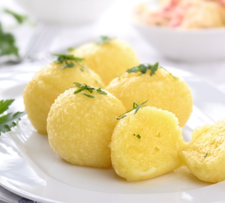 Auf einem weißen Teller liegen mehrere hausgemachte Kartoffelknödel, die mit Petersilie bestreut sind. | © Shutterstock / Karl Allgaeuer