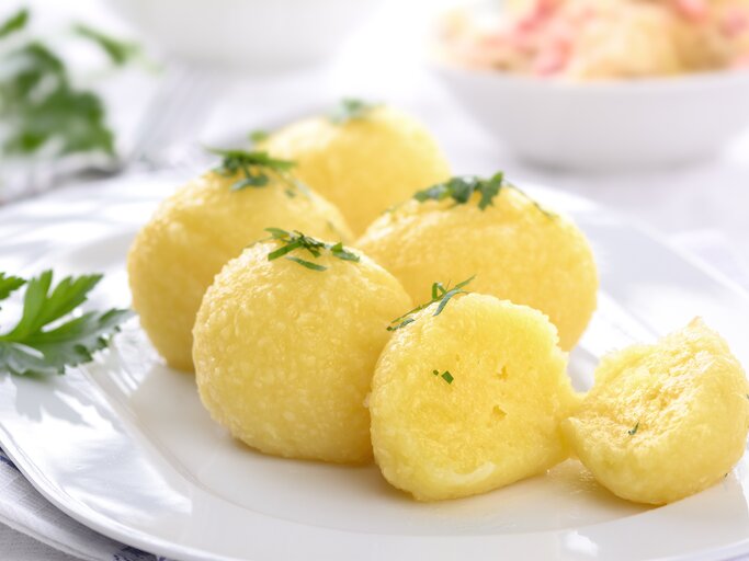 Auf einem weißen Teller liegen mehrere hausgemachte Kartoffelknödel, die mit Petersilie bestreut sind. | © Shutterstock / Karl Allgaeuer