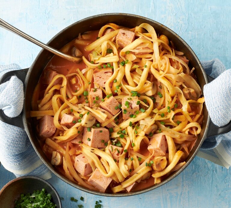 In einem Topf ist ein bayerischer Spätzle-Topf mit Leberkäse, Champignons und Kohl angerichtet. Daneben steht geriebener Käse. | © StockFood Studios / Brachat, Oliver; 