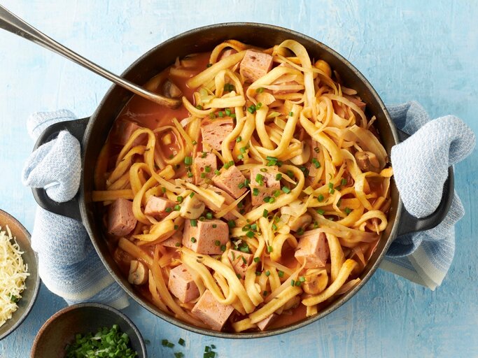 In einem Topf ist ein bayerischer Spätzle-Topf mit Leberkäse, Champignons und Kohl angerichtet. Daneben steht geriebener Käse. | © StockFood Studios / Brachat, Oliver; 
