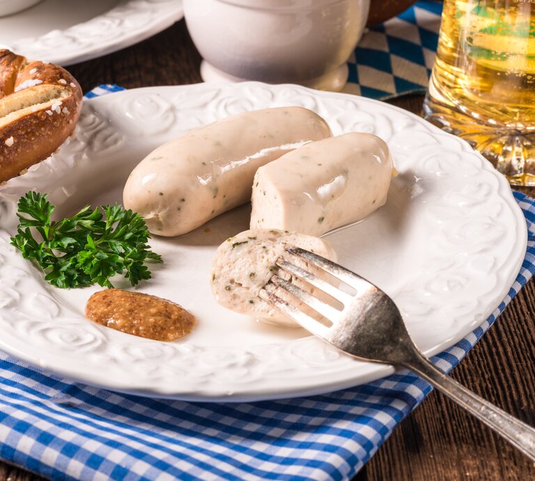 Ein Teller mit veganen Weiswürsten, süßem Senf und einer Brezel, daneben ein Glas Bier. | © Shutterstock/ Dar1930