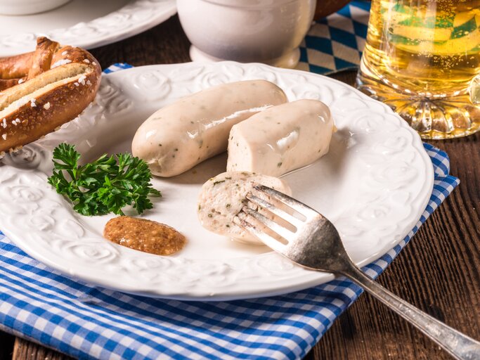 Ein Teller mit veganen Weiswürsten, süßem Senf und einer Brezel, daneben ein Glas Bier. | © Shutterstock/ Dar1930