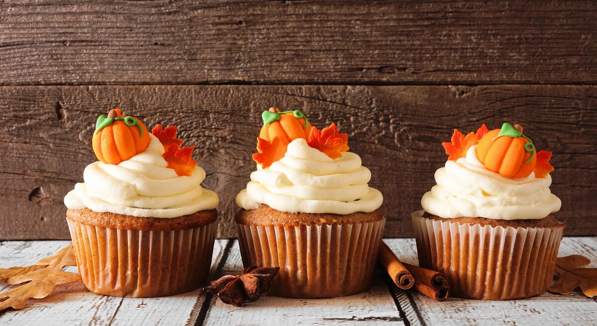 Drei Kürbis-Cupcakes verziert mit kleinen Kürbissen und Ahornblättern aus Marzipan, daneben Zimtstangen und Anissterne.