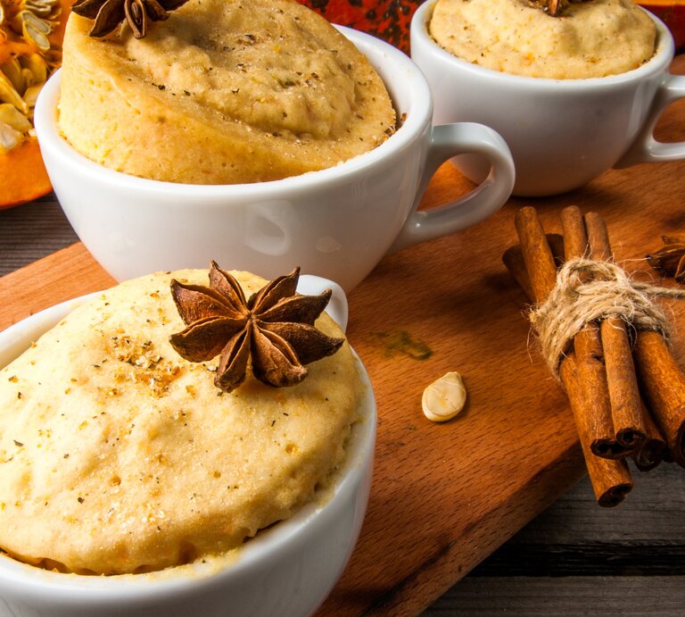 Drei Tassen mit dem Kuchen auf einem braunen Holzbrett. Daneben Kürbisspalten und Sternanis. Alles auf einem rustikalen Holztisch von schräg oben fotografiert. | © SHutterstock/ Rimma Bondarenko 