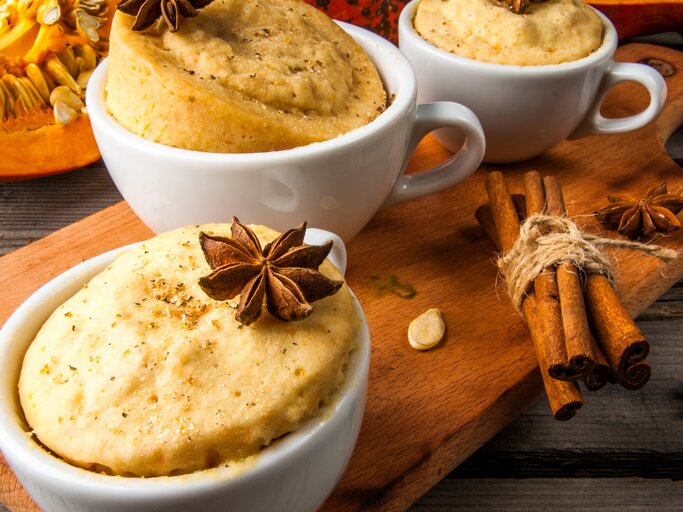 Drei Tassen mit dem Kuchen auf einem braunen Holzbrett. Daneben Kürbisspalten und Sternanis. Alles auf einem rustikalen Holztisch von schräg oben fotografiert. | © SHutterstock/ Rimma Bondarenko 