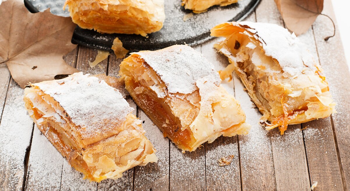 Leckerer Kürbis-Strudel auf einem Holztisch mit Herbstblättern von schräg oben fotografiert.