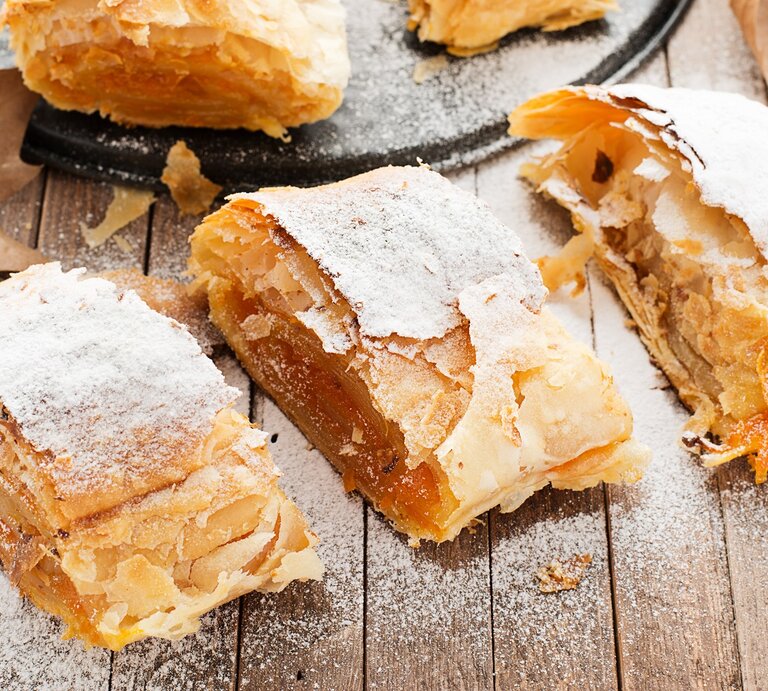 Leckerer Kürbis-Strudel auf einem Holztisch mit Herbstblättern von schräg oben fotografiert. | © Shutterstock/ nelea33